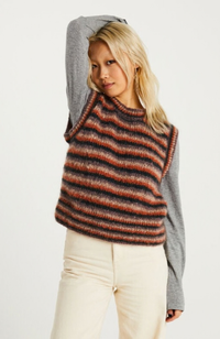 Blonde model in gray long sleeve shirt and cream pants wearing a multicolored knit vest.