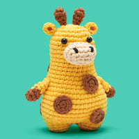 A crocheted plush giraffe toy in yellow with brown spots, standing against a solid teal background.