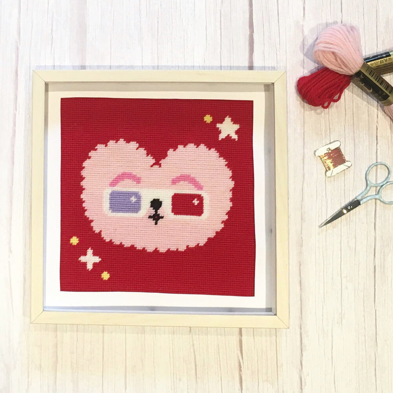 Framed needlepoint heart design with cartoon face on a red background, 