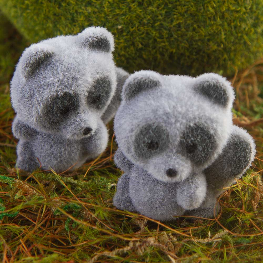 Two gray fuzzy raccoon miniatures on a grassy surface outdoors.