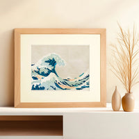 Framed needlepoint artwork with a wave design resting on a white shelf against a tan background