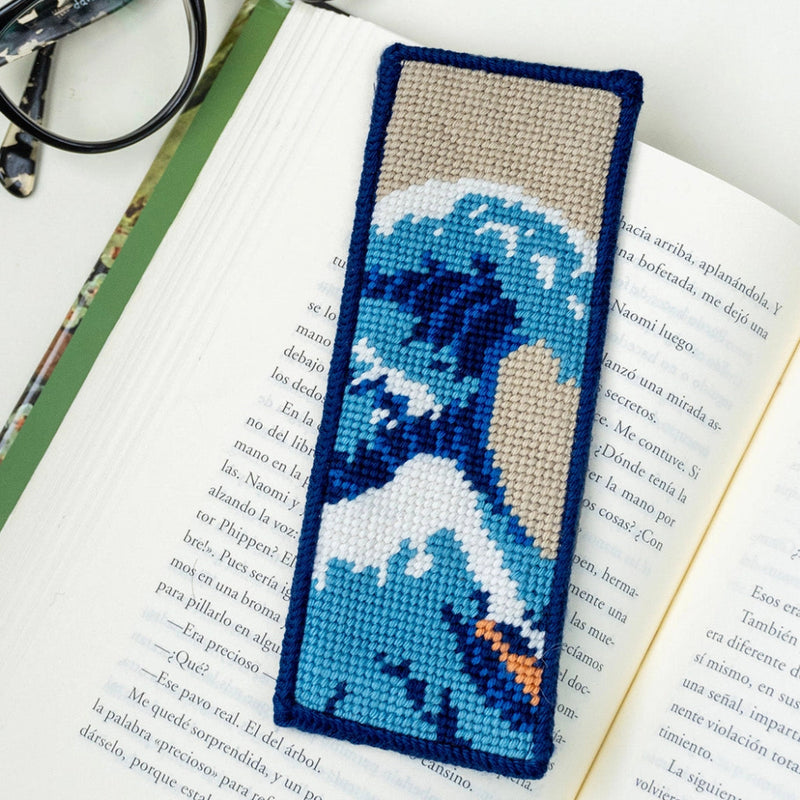 Needlepoint bookmark with a wave design on an open book with glasses on a white background