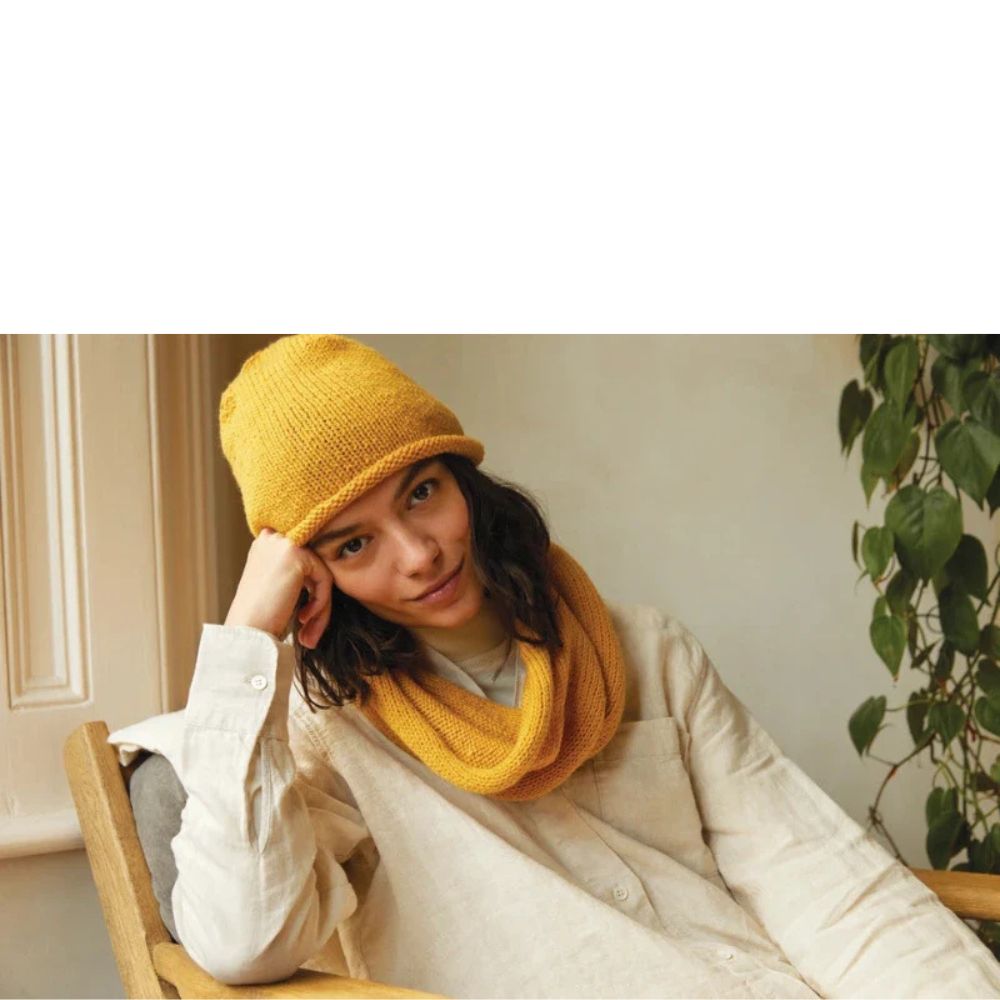 Person wearing a yellow knitted hat and scarf sitting indoors.