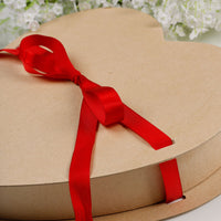 Cardboard gift box with a red ribbon tied in a bow against a blurred floral background