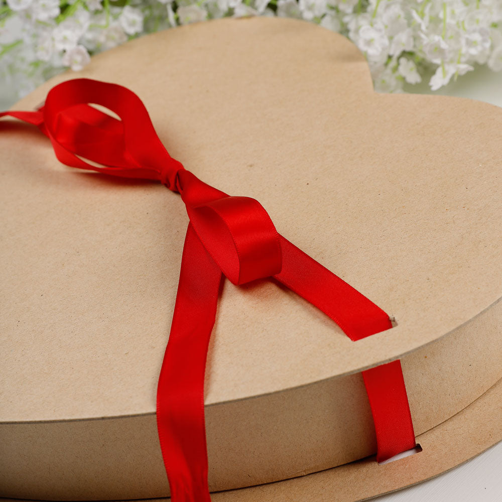 Cardboard gift box with a red ribbon tied in a bow against a blurred floral background