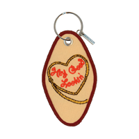 Tan embroidered motel-style keychain that reads "hey good lookin" inside a heart-shaped rope