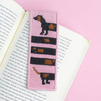 Needlepoint bookmark with a dog design on an open book against a pink background