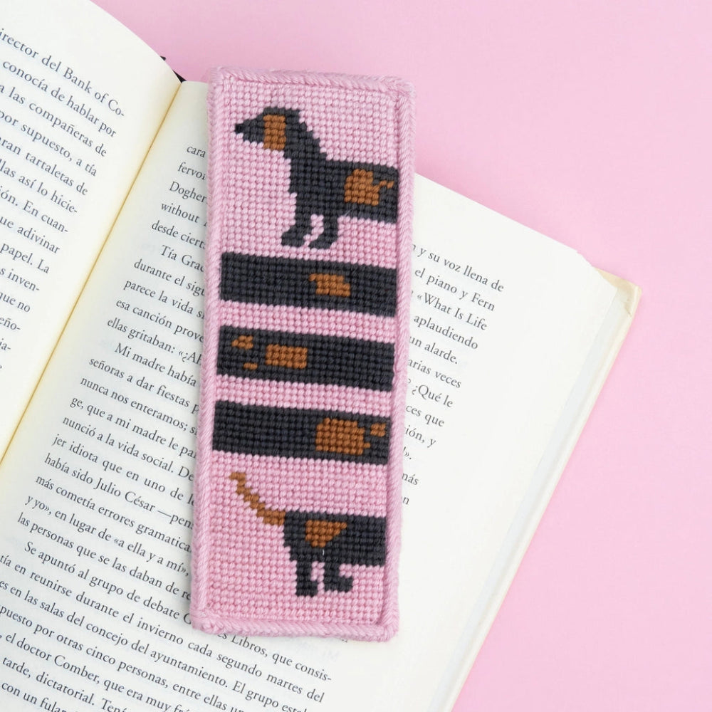 Needlepoint bookmark with a dog design on an open book against a pink background