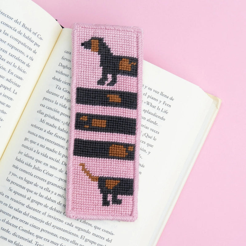 Needlepoint bookmark with a dog design on an open book against a pink background