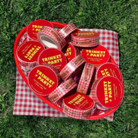 Red hot dog container with 'Trinket Party' branding on a checkered cloth on grass