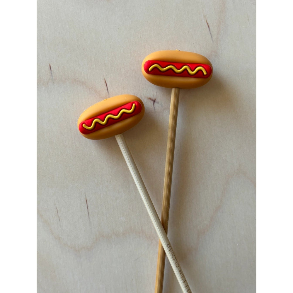 Two hot dog-shaped silicone ends on needles against a light background.