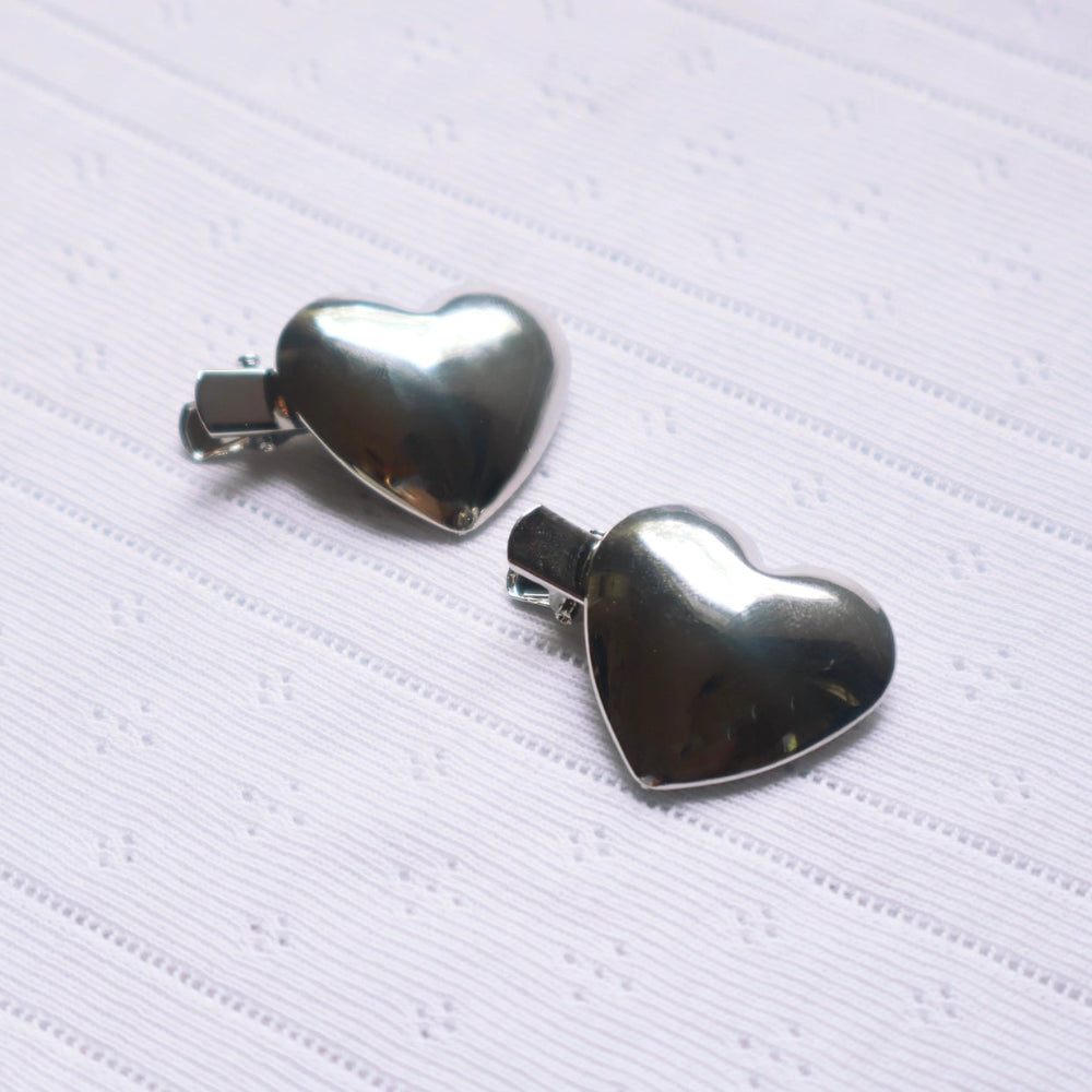 Silver heart-shaped hair clips on a textured white background