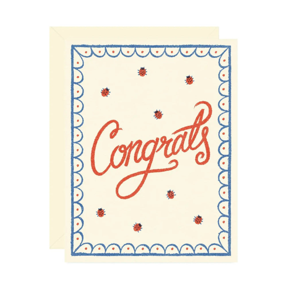 A beige colored card with scattered illustrated ladybugs and a blue and red scalloped border. Red text in the middle reads "Congrats". A matching envelope is behind the card. 