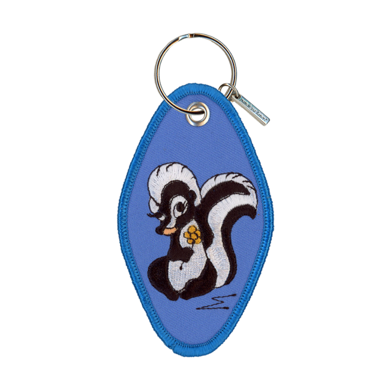 Blue embroidered motel-style keychain featuring a skunk design