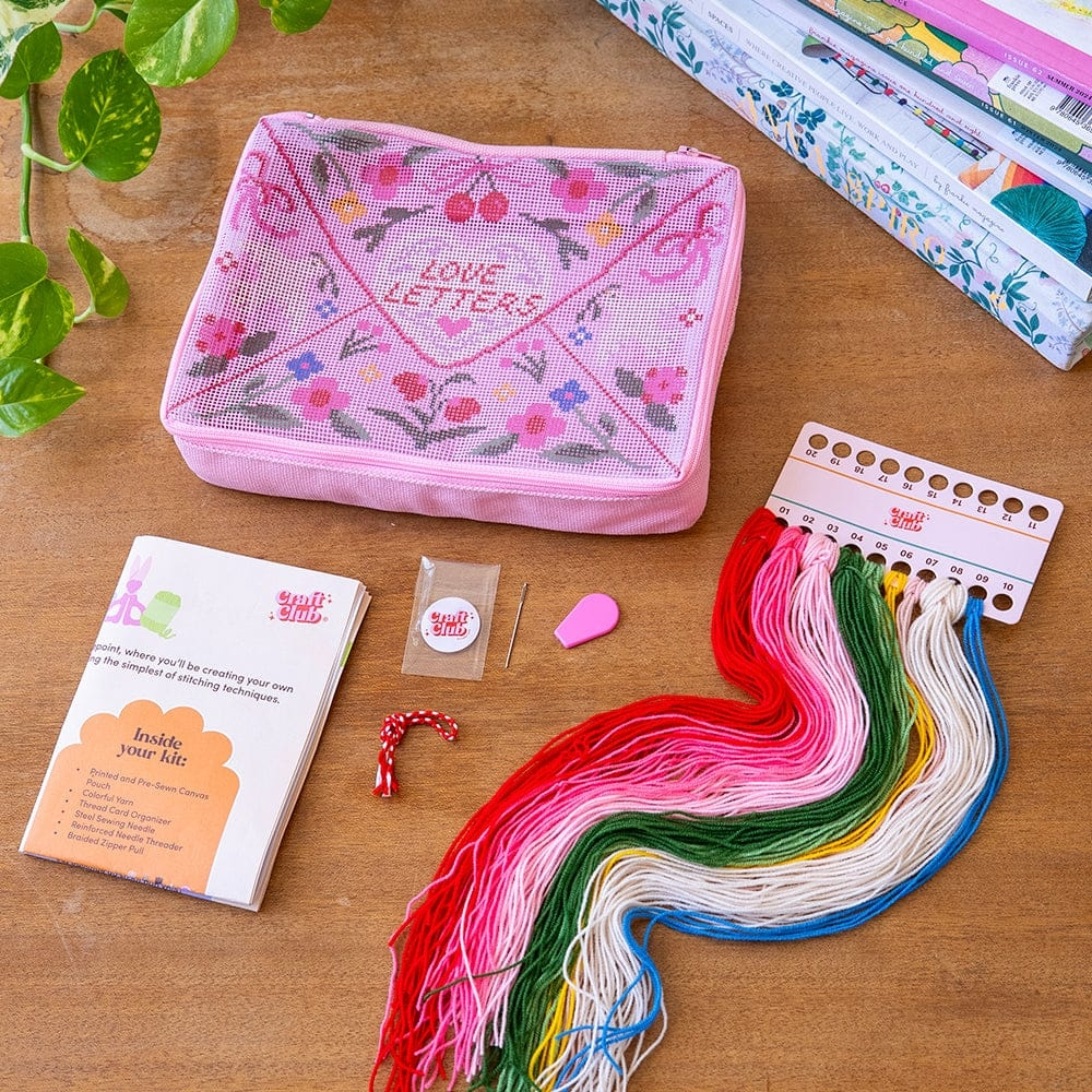 The kit for the needlepoint pouch showing all the included materials like colorful yarn, a needle, pre-sewn pouch and instructions