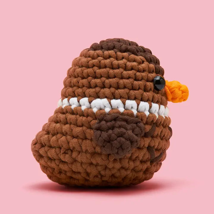 side view of a brown crocheted duck on a pink background