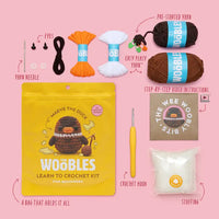 Content of the kit and the packaging including: yarn needle, eyes, easy-peasy yarn, pre-started yarn, instructions, a crochet hook and stuffing on a pink background