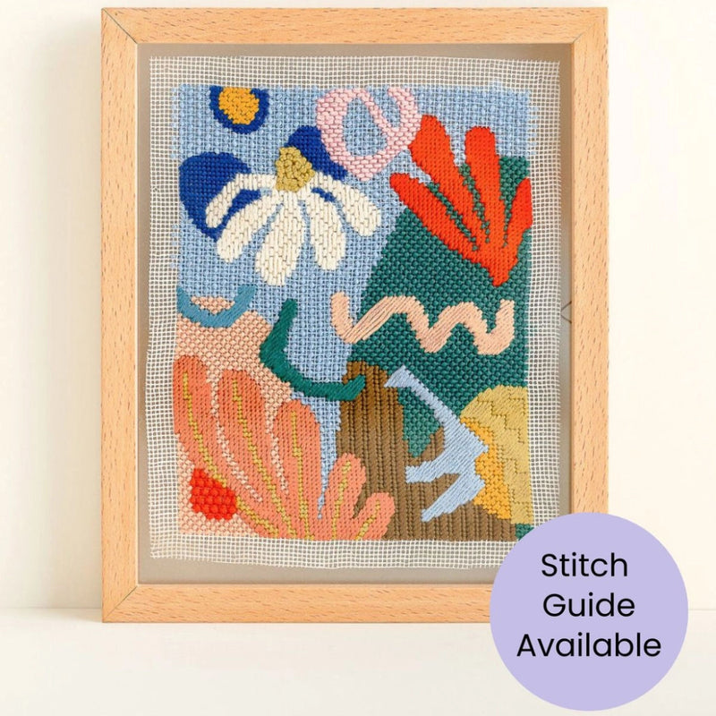Framed needlepoint artwork with colorful abstract design on a white wall.