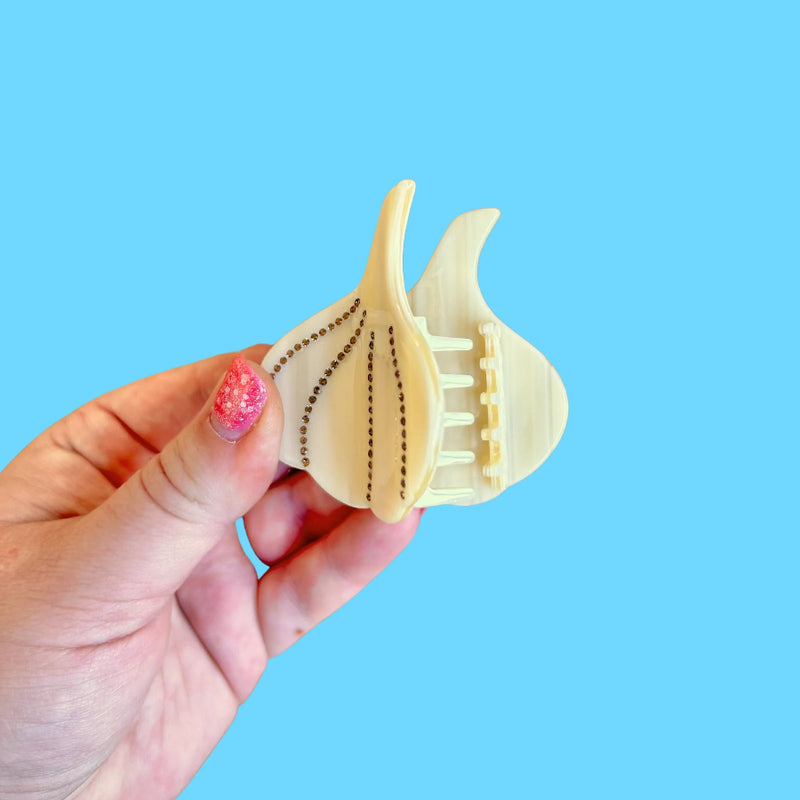Hand with pink nail polish holding a garlic shaped hair claw in front of a blue background.