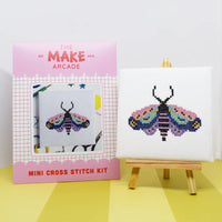 Make Arcade mini cross stitch kit with a completed  moth cross stitch on an easel against a white background.