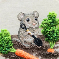 Closeup of embroidered mouse with a shovel digging up carrots