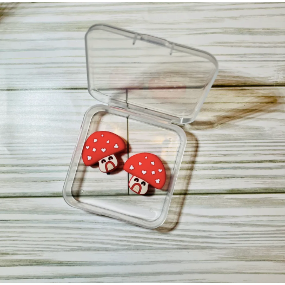 Red mushroom-shaped point protectors in a clear jewelry case on a wooden surface