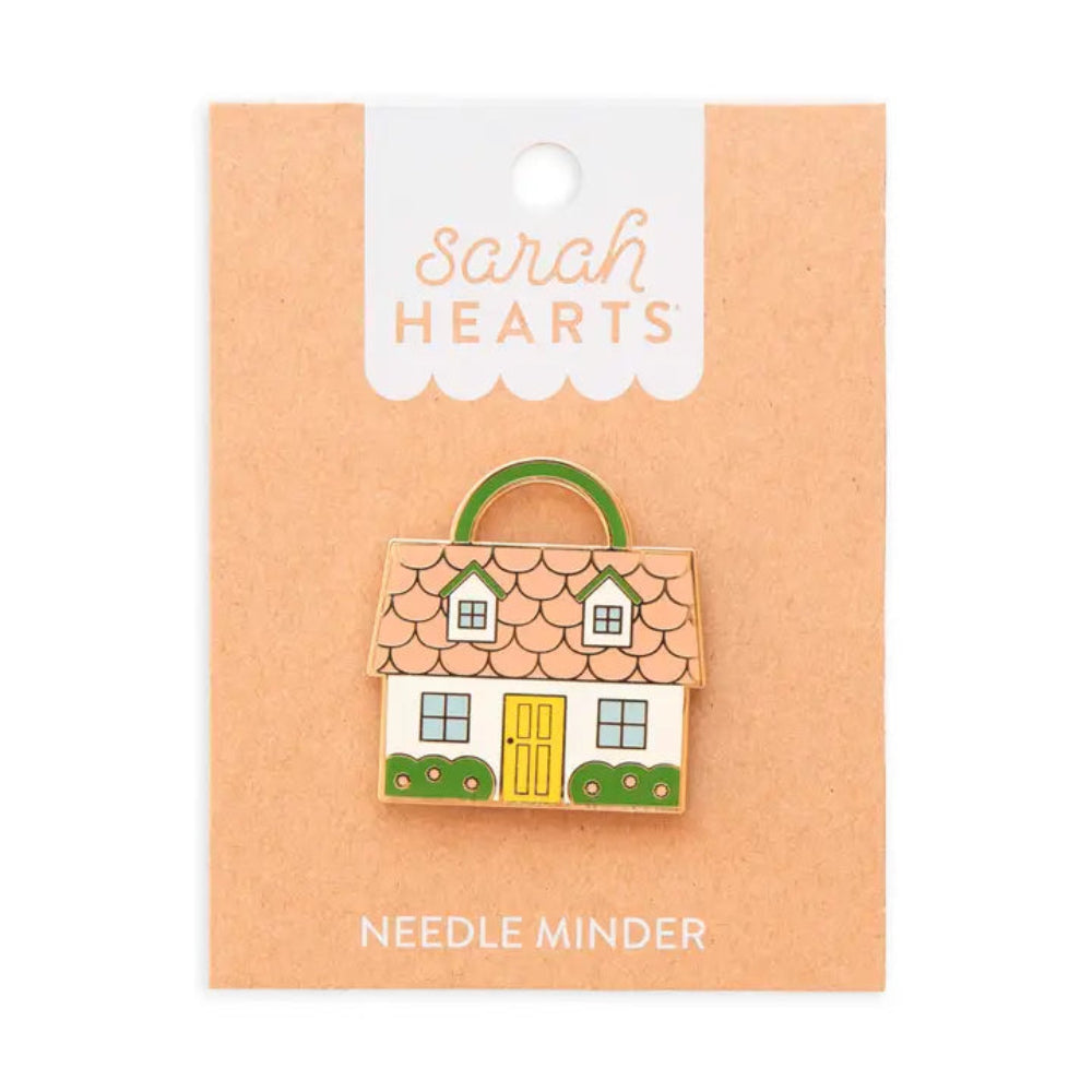 A needle minder shaped like a house with a  pink roof, yellow door, and green shrubs on brown Sarah Hearts packaging. 
