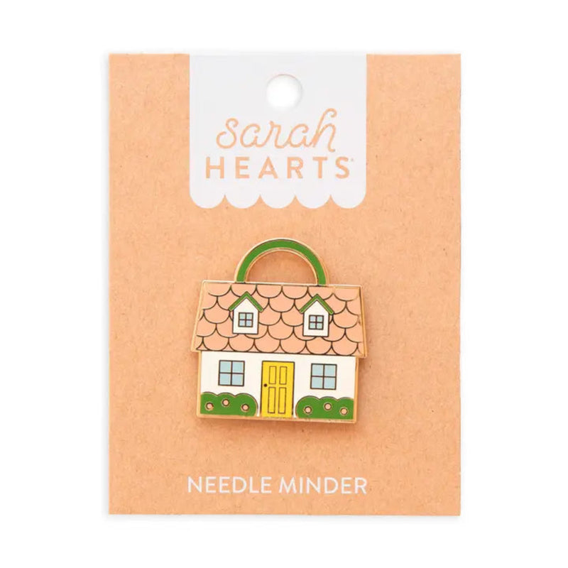 A needle minder shaped like a house with a  pink roof, yellow door, and green shrubs on brown Sarah Hearts packaging. 