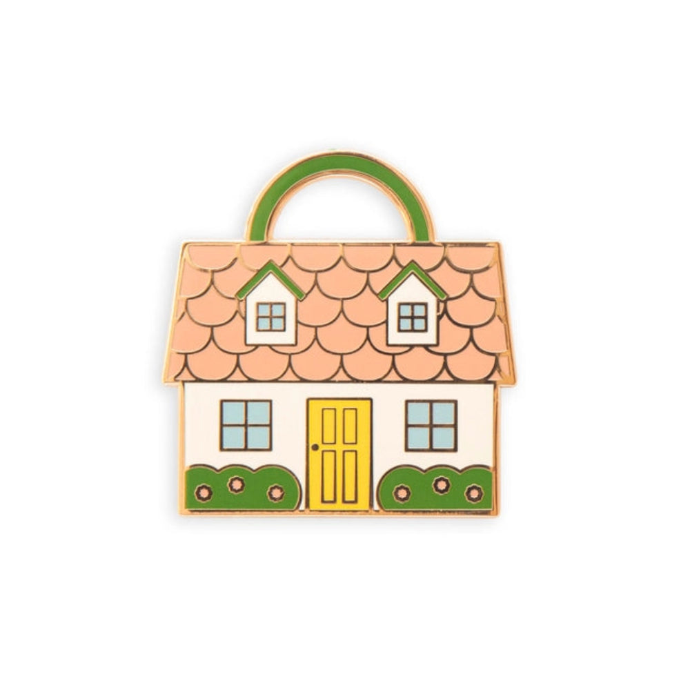 A needle minder shaped like a house with a pink roof, yellow door, and green shrubs on a white background