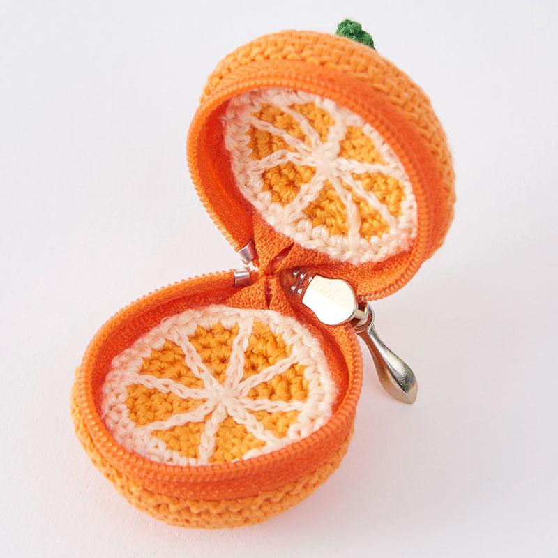 A crocheted orange-shaped zipper case shown open on a plain white background, with orange and white crochet slice details and a small green top accent.