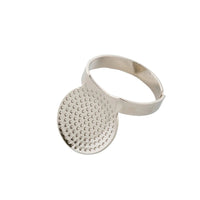 A silver-toned ring featuring a large, flat oval disc with a textured, dimpled surface, attached to a smooth band, shown on a plain white background.