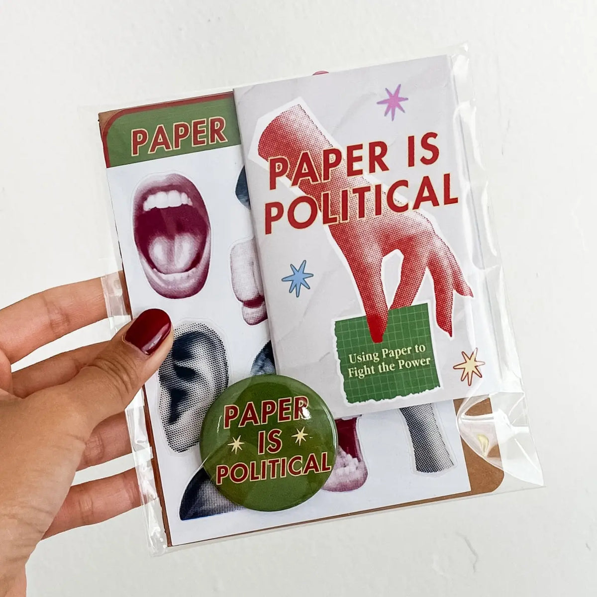 Hand holding clear plastic bag containing sticker sheet and button that both say "paper is political."