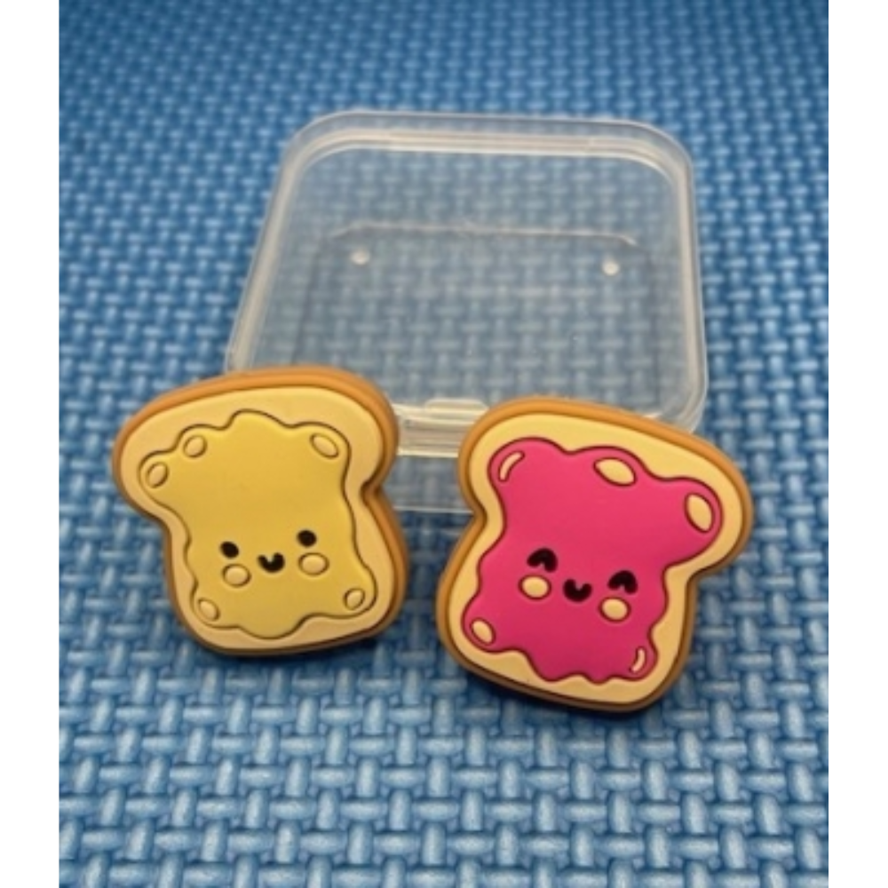 Silicone bread, one with peanut butter, one with jelly, point protectors with clear box on blue woven textured background.
