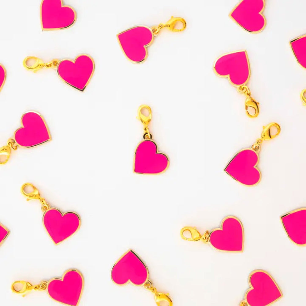 Pink heart charms with golden borders and clasps are scattered on a white background.