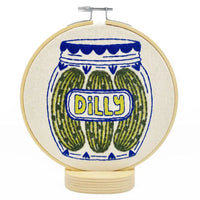 Embroidery hoop with a design of pickles in a jar labeled 'Dilly'.