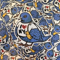 Pile of stickers in the shape of a blue pigeon wearing an I heart NY shirt and carrying a tote bag.