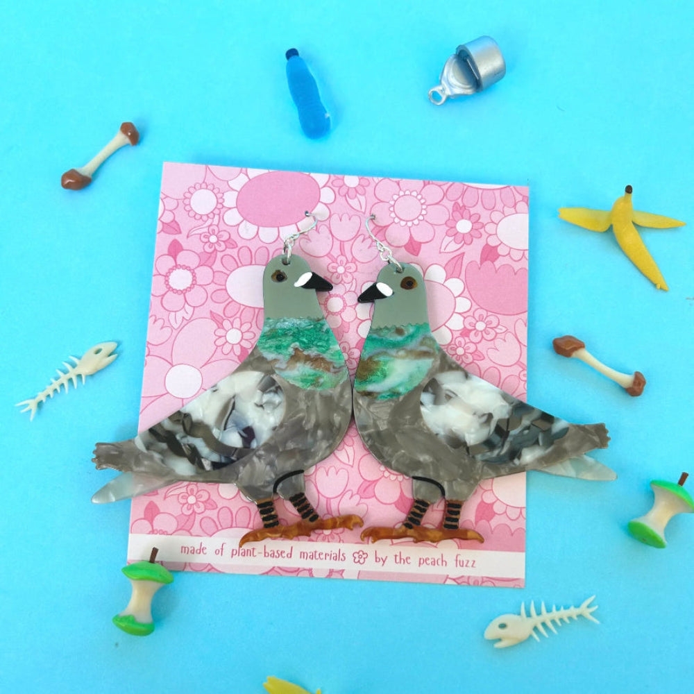 Flat acetate earrings in the shape of a pigeon, attached to a pink backng card with silver ear hooks.