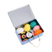 Colorful yarn balls and a pom-pom making tools in an open metal box on a white background