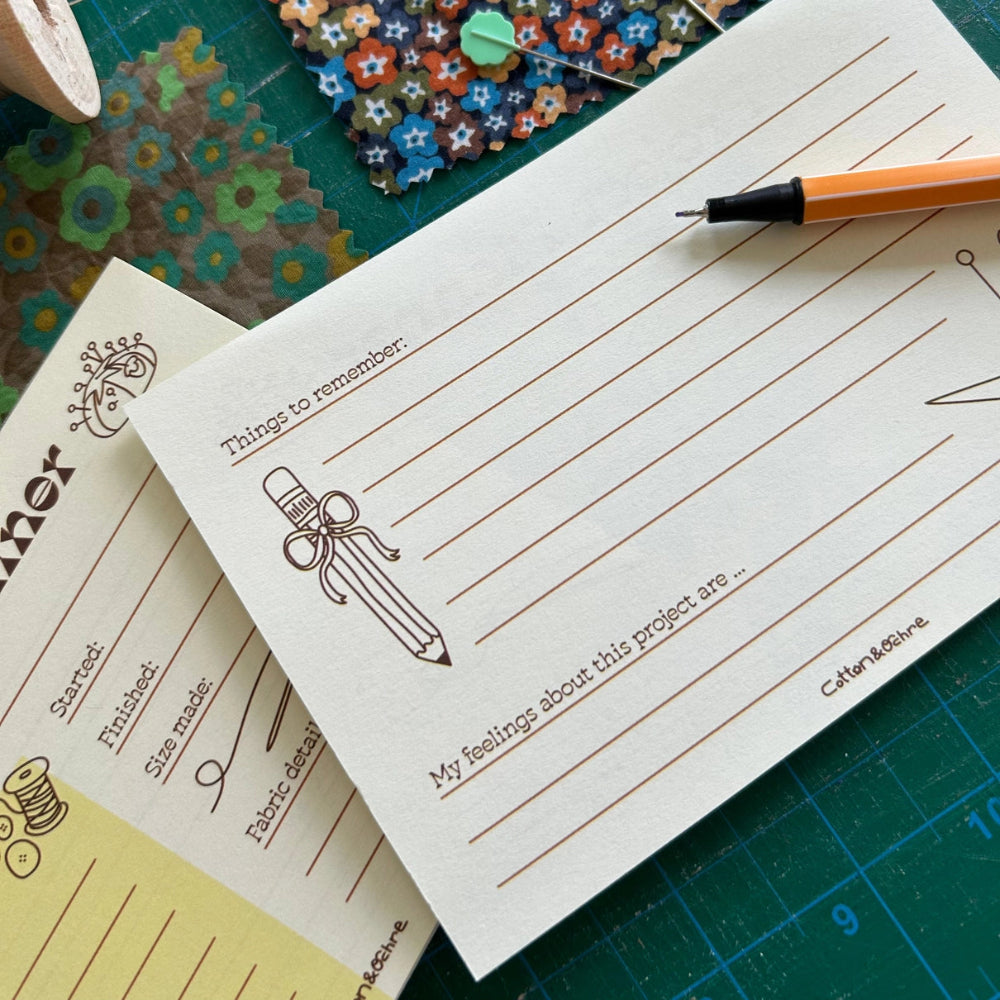 Notebook with lined pages and a pen on a green cutting mat with sewing materials.