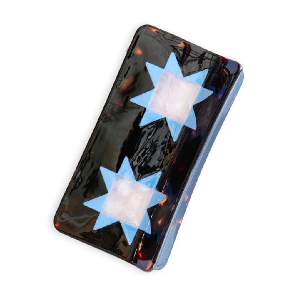 A tortoise hair clip adorned with two blue quilt star shapes, against a white  background. 