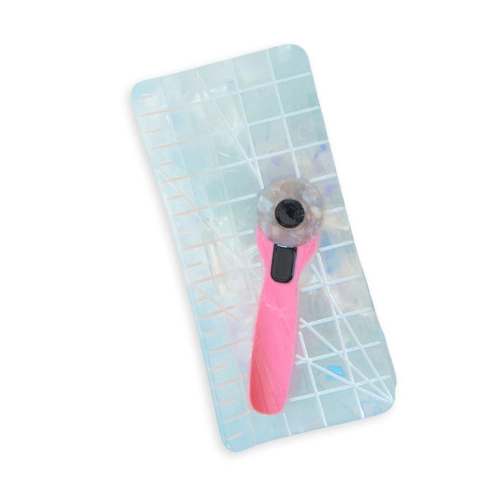 A holographic cutting mat with a pink rotary cutter design attached, set against a white background.