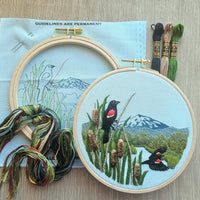 Embroidery hoops with embroidered red winged blackbirds and landscape on a textured surface. 