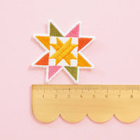Colorful sawtooth quilt block patch on a pink background with a ruler for scale.