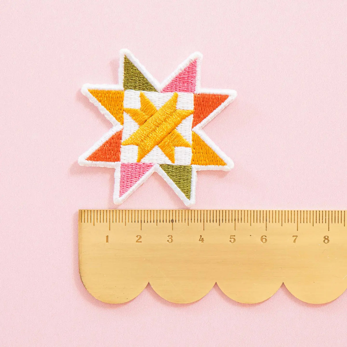 Colorful sawtooth quilt block patch on a pink background with a ruler for scale.