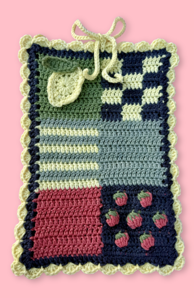 Crocheted book sleeve with patchwork pattern on a pink background