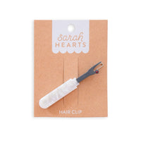 Hair clip shaped like a seam ripper with a pearlized handle on  "Sarah Hearts" packaging. 