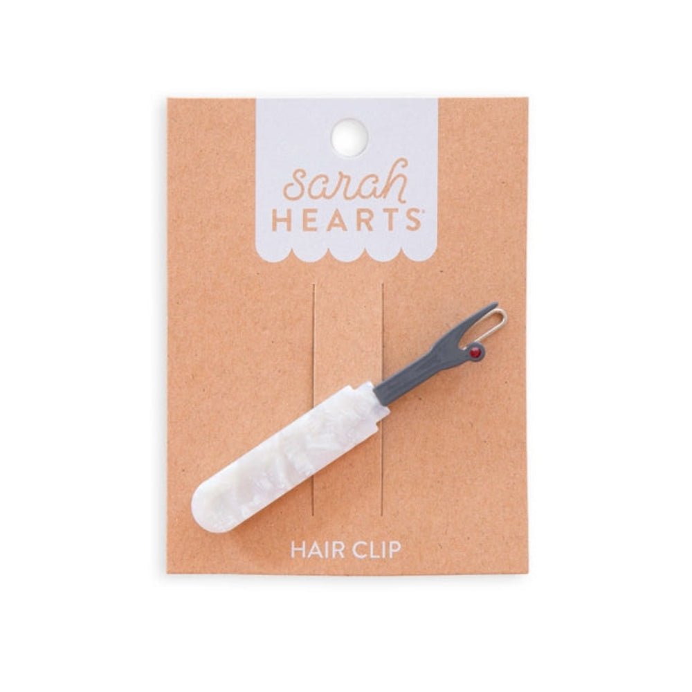 Hair clip shaped like a seam ripper with a pearlized handle on  "Sarah Hearts" packaging. 