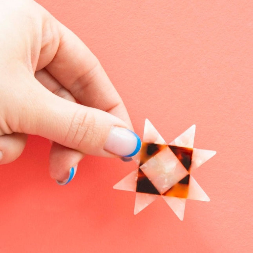 Hand holding a star-shaped object with a geometric pattern against a pink background