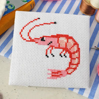 Cross-stitched shrimp design on white fabric