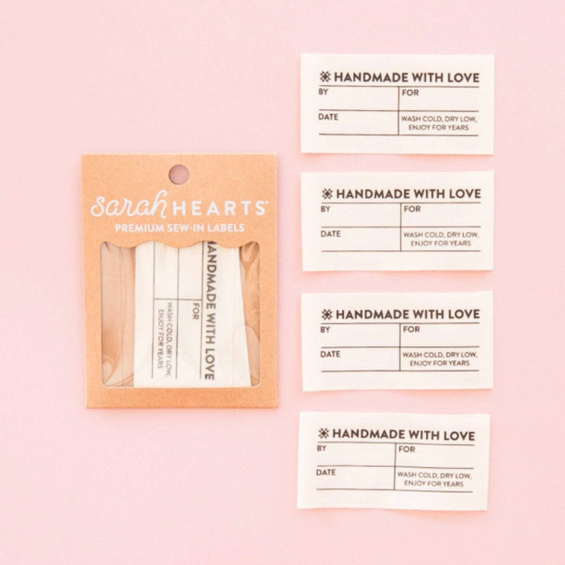 Cream-colored fabric labels, titled "Handmade with Love" with spaces for "By," "Date," and "For." Instructions: "Wash cold, dry low. Enjoy for Years" in "Sarah Hearts" packaging